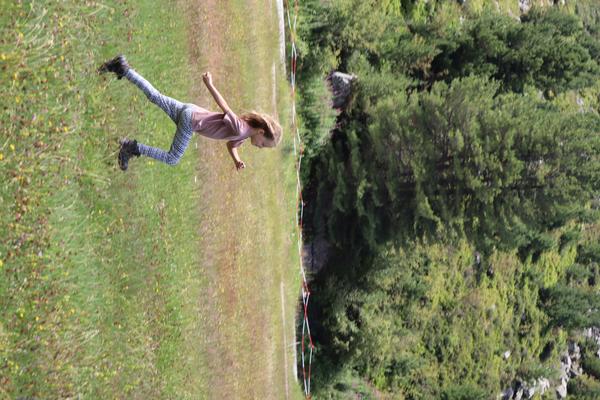 A young child is captured mid-stride, running or jumping across a sunlit grassy field